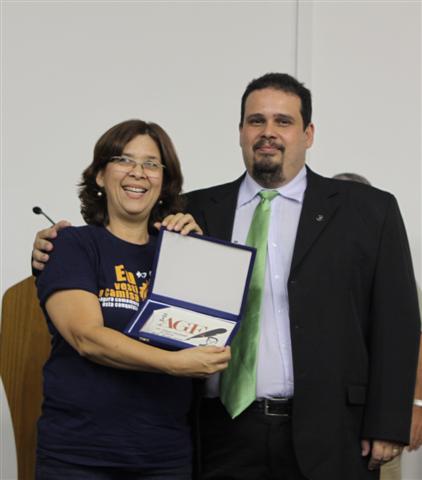 A representante da aluna Camila Macedo do Colégio Objetivo, recebe o troféu de 1º lugar das mãos do neto do Poeta Lydio Martins Corrêa.